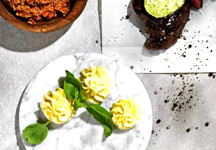 Knoblauchbutter rezept: Ein Steak mit Kräuterbutter, dazu Kartoffelröschen und eine Schüssel mit würziger Butter.