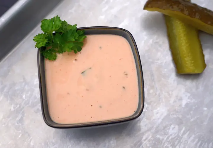 Cremige In-N-Out Burger Sauce in einer Schale, garniert mit Petersilie. Daneben liegen zwei saftige Gurkenscheiben.