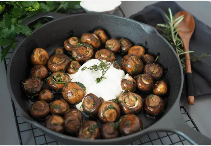 Gebratene Champignons mit Kräutern und cremiger Sauce in einer Gusseisenpfanne. Perfekt für leckere Champignons Rezepte.