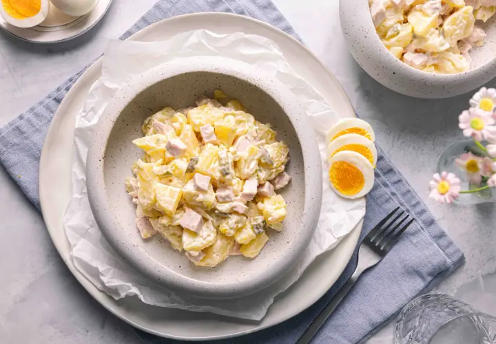 Ein cremiger Kartoffelsalat mit Mayonnaise, Schinken und Gewürzgurken, serviert mit gekochten Eiern. Ein klassisches Kartoffelsalat Rezept mit Mayonnaise.