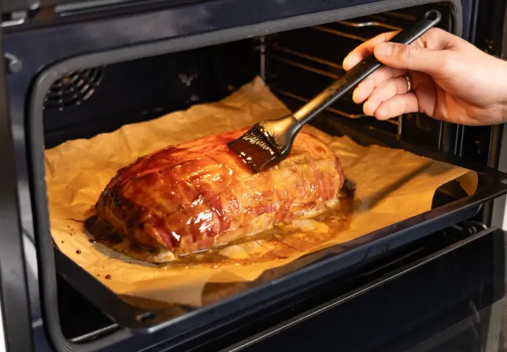 Ein Braten, umwickelt mit Bacon, wird im Backofen mit einer Glasur bestrichen. Die Bacon-Bomb-Zubereitung im Ofen ist fast fertig.