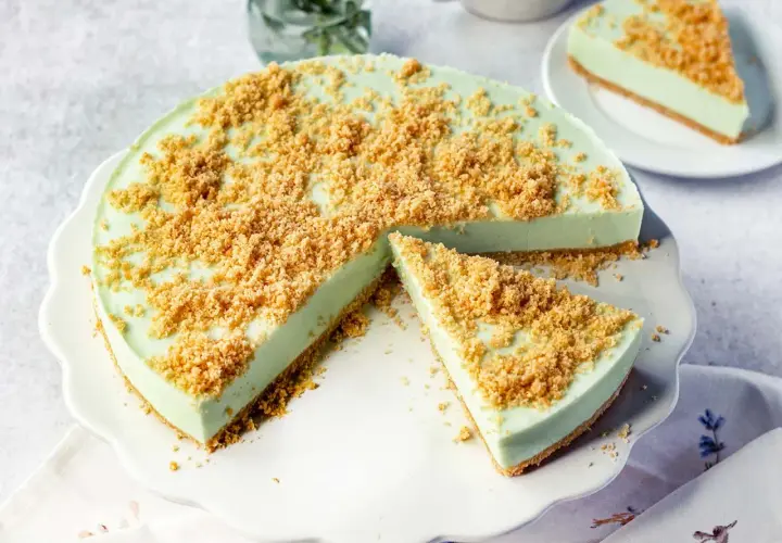 Eine cremige Philadelphia Torte Waldmeister mit knuspriger Streuselhaube, ein Stück ist bereits angeschnitten.