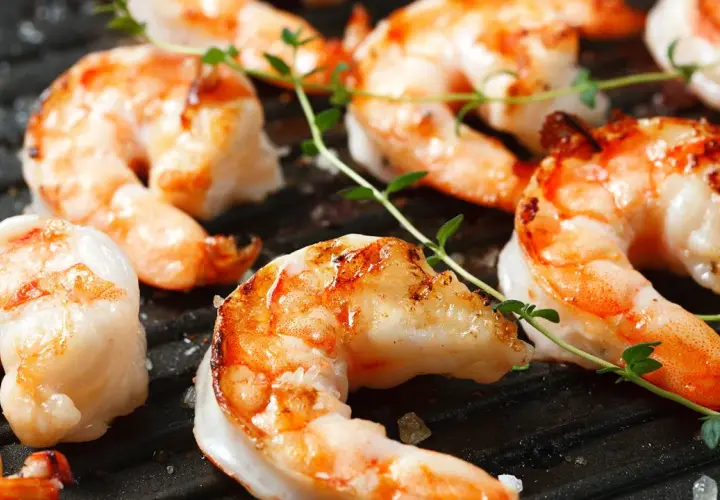 Saftige black tiger Garnelen grillen auf einer heißen Grillplatte, garniert mit frischem Thymian.