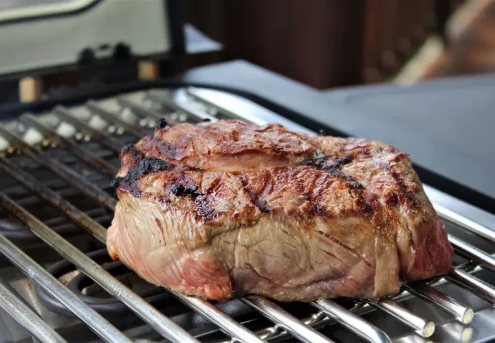 Ein saftiges Steak brutzelt auf einem Elektrogrill. Die Grillstreifen sind deutlich sichtbar, und das Fleisch ist perfekt gebräunt.