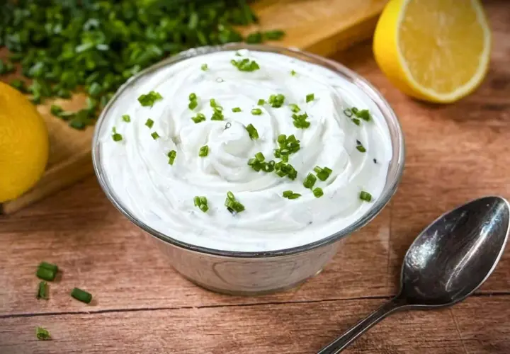 Cremige Sour Cream, frisch zubereitet, mit Schnittlauch garniert. Dazu Zitrone und ein Löffel – perfekt zum Sour Cream selber machen.