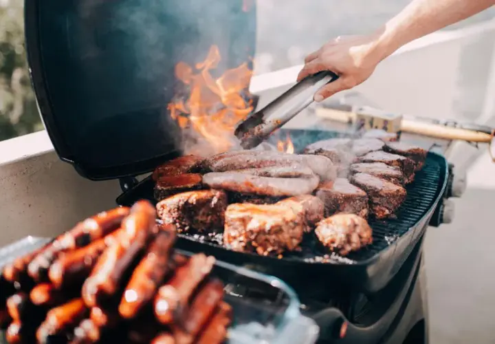 Fleisch und Würstchen brutzeln auf einem Grill auf dem Balkon. Die Frage, ob man auf dem Balkon grillen darf, wird hier mit Genuss beantwortet.