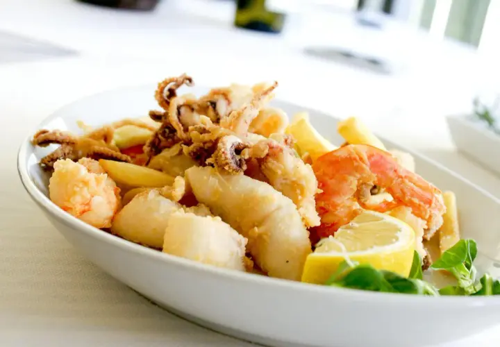 Knuspriges Fritto Misto mit Garnelen, Tintenfischringen und Fischstücken, garniert mit Zitrone und frischen Kräutern.