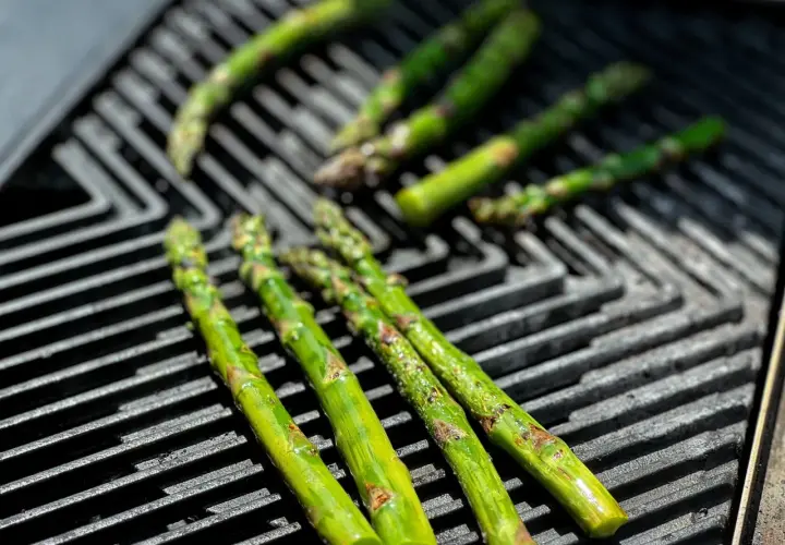 Frischer Spargel grillen auf einem Gasgrill. Die grünen Stangen werden von der Hitze leicht gebräunt und verströmen ein köstliches Aroma.