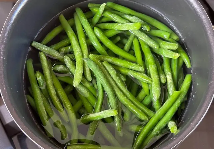 Grüne Bohnen kochen in einem Topf mit Wasser. Sie sind frisch und leuchtend grün, bereit für eine gesunde Mahlzeit.