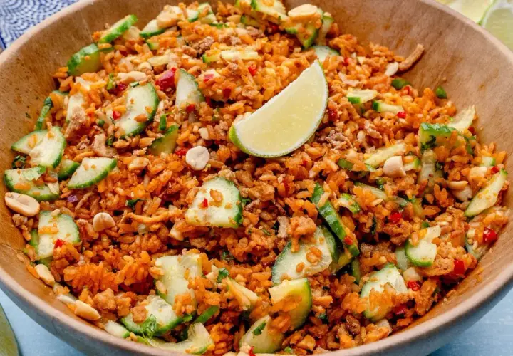 Ein Schüssel mit knusprigem Reis Salat, garniert mit Gurkenscheiben, Erdnüssen und Limettenspalten.