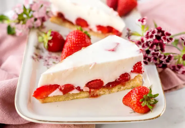 Ein Stück Erdbeerkuchen mit weißer Creme und frischen Erdbeeren auf einem Teller.