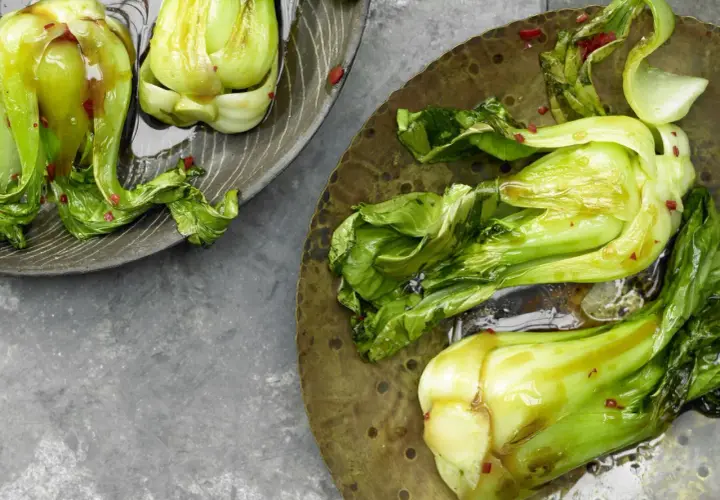 Zwei Teller mit gedünstetem Pak Choi, glänzend von einer Sauce und bestreut mit roten Chiliflocken.