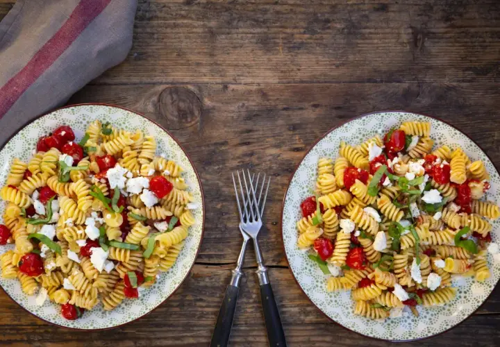 Zwei Teller mit leckeren schnellen Salaten ohne Mayo: Fusilli mit Kirschtomaten, Feta und Basilikum auf rustikalem Holztisch.