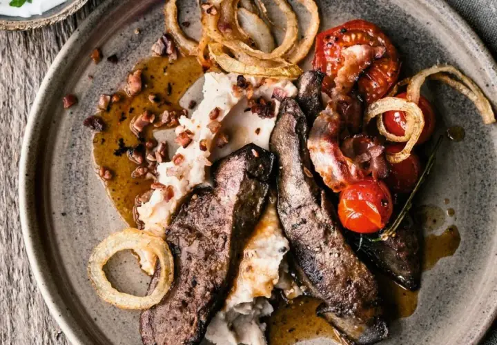 Herzhaftes leber braten mit Kartoffelpüree, Speck, Kirschtomaten und Röstzwiebeln auf einem rustikalen Teller.