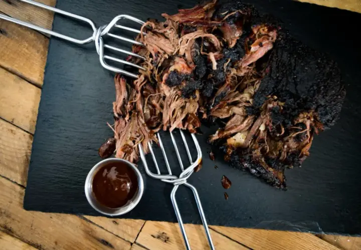 Zartes pulled beef mit dunkler Kruste, serviert mit BBQ-Sauce auf einem Schieferbrett.