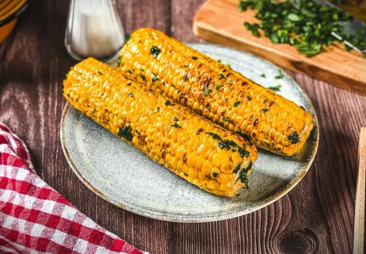 Zwei goldgelbe Maiskolben, perfekt gegrillt und mit Kräutern bestreut, liegen auf einem Teller. Ein Genuss für alle Sinne!
