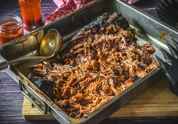 Saftiges pulled pork, frisch aus dem Gasgrill, in einer Metallschale mit Sauce und Fleischgabel.