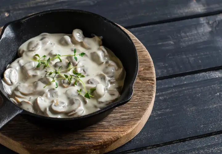 Cremige Champignon Rahmsauce in einer Gusseisenpfanne, garniert mit frischem Thymian.