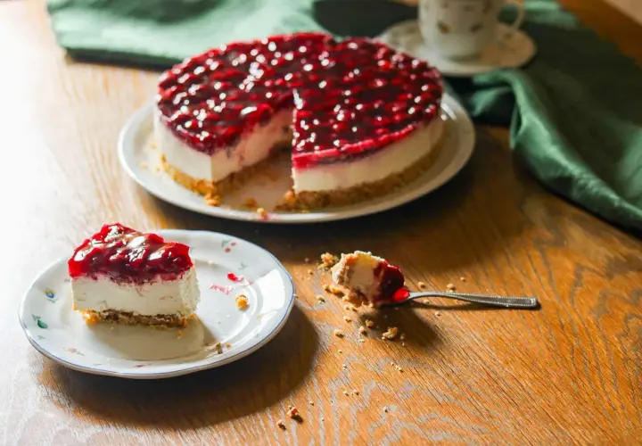 Ein köstlicher Kuchen ohne Backen mit Kirschtopping. Ein Stück auf einem Teller, ein Löffel mit einem Bissen daneben.