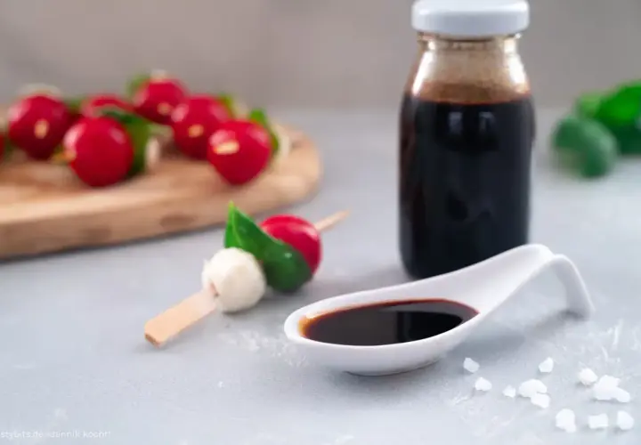 Ein Löffel mit dunkler balsamico creme, daneben eine Flasche und Radieschen-Mozzarella-Spieße.