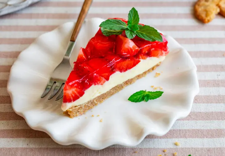 Ein Stück Erdbeerkuchen mit Keksboden, schnell und ohne Backen zubereitet. Frisch, fruchtig und mit Minze garniert.
