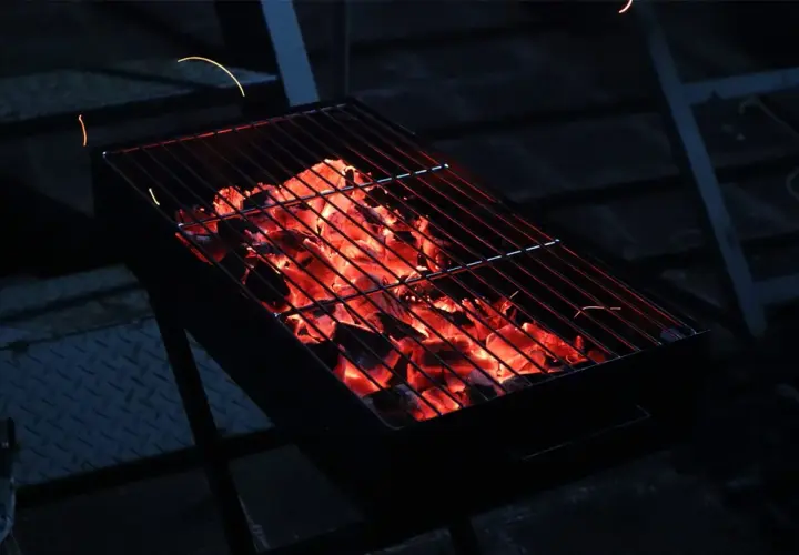 Glühende Kohlen unter dem Rost versprechen ein gemütliches Grillen mit Holzkohle. Funken tanzen in der Dunkelheit.