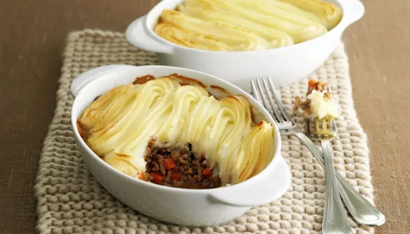 Zwei Auflaufformen mit goldbraunem Shepherd's Pie, bedeckt mit kunstvoll gespritztem Kartoffelpüree.