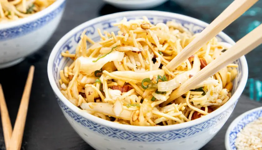 Ein Schüsselchen mit friss dich dumm salat, Nudeln, Gemüse und Erdnüssen, bereit zum Genießen mit Stäbchen.