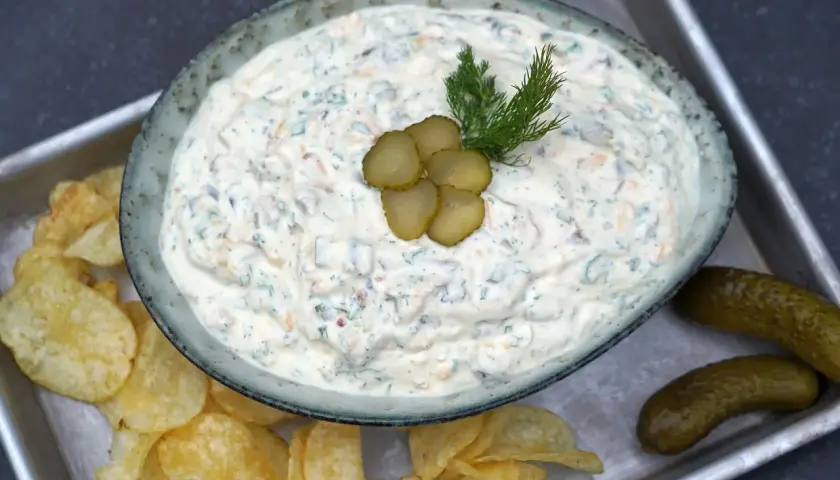 Cremiger blue cheese dip mit Dill und Gurkenscheiben, serviert mit Kartoffelchips und Gewürzgurken.