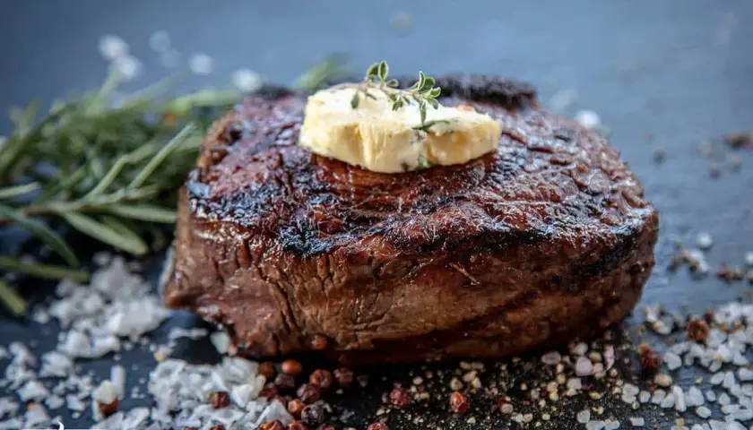 Perfekt gegrilltes Entrecôte mit Kräuterbutter, umgeben von grobem Salz und Pfefferkörnern. Ein Fest für Fleischliebhaber!