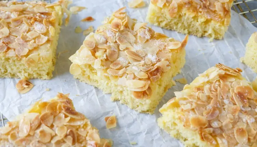 Saftiger Buttermilch Kuchen mit Mandelsplittern und Zucker bestreut, auf Backpapier und einem Gitter angerichtet.