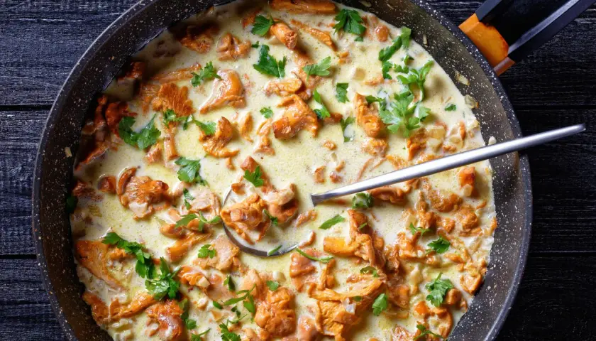 Pfifferlinge in cremiger Rahmsauce, garniert mit Petersilie, in einer Pfanne. Ein Löffel ragt aus der köstlichen Speise.
