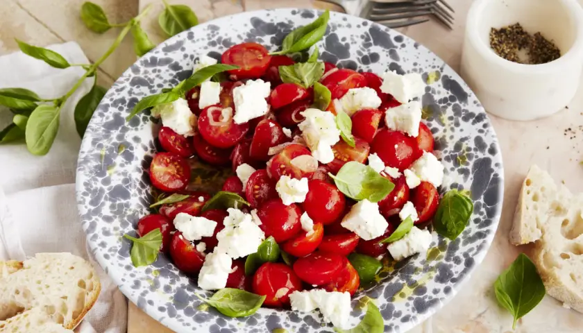 Frischer tomatensalat mit feta, garniert mit Basilikum. Dazu gibt es knuspriges Brot.