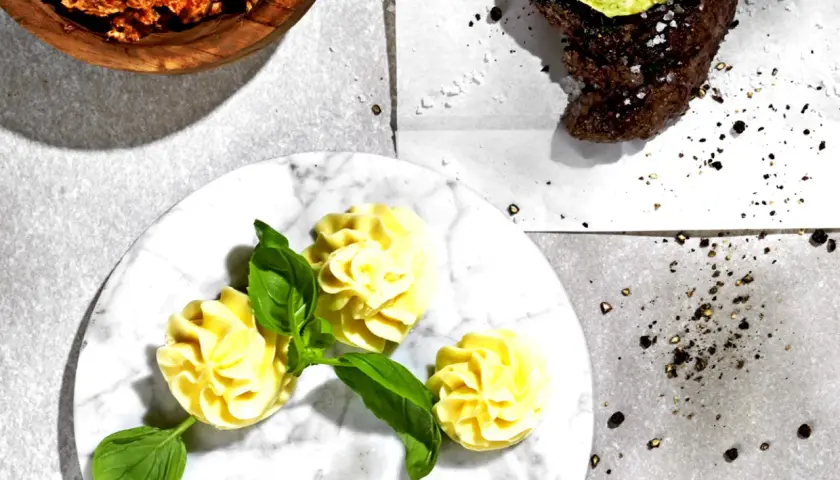 Knoblauchbutter rezept: Ein Steak mit Kräuterbutter, dazu Kartoffelröschen und eine Schüssel mit würziger Butter.