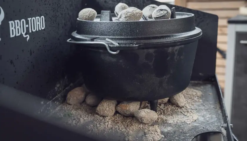 Ein Dutch Oven auf einem Gasgrill, bereit für ein köstliches Outdoor-Abenteuer. Glühende Kohlen sorgen für die perfekte Hitze.