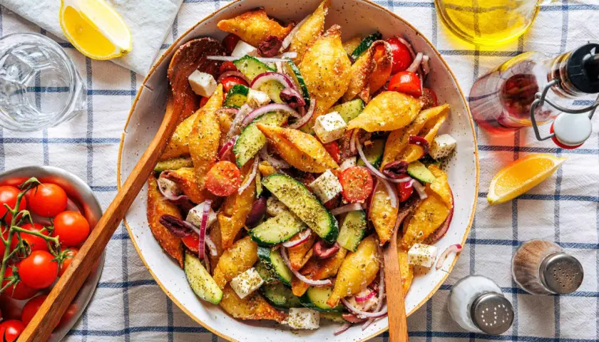 Ein bunter Nudelsalat mal anders: knusprige Muschelnudeln mit Gurke, Tomaten, Feta und roten Zwiebeln, garniert mit Kräutern.