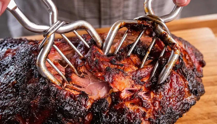 Zwei Fleischgabeln zerreißen ein saftiges, dunkles Pulled Pork. Perfekt für leckere Rezepte mit fertigem Pulled Pork.