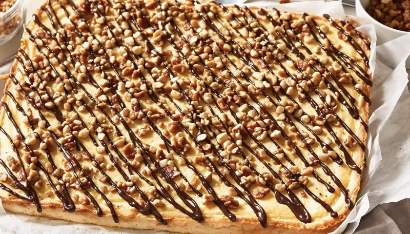 Ein rechteckiger "Friss dich dumm Kuchen" mit cremiger Füllung, garniert mit Nüssen und Schokoladensauce.