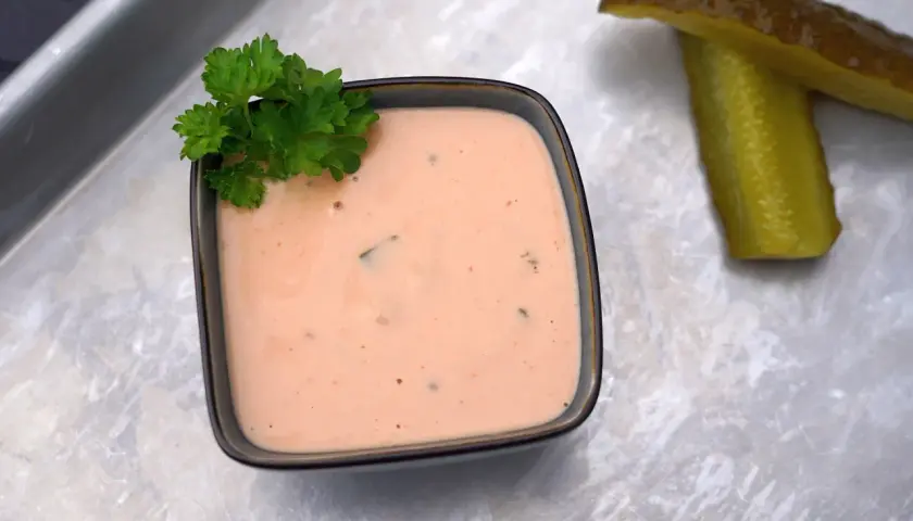 Cremige In-N-Out Burger Sauce in einer Schale, garniert mit Petersilie. Daneben liegen zwei saftige Gurkenscheiben.