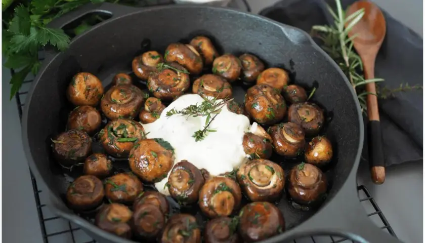 Gebratene Champignons mit Kräutern und cremiger Sauce in einer Gusseisenpfanne. Perfekt für leckere Champignons Rezepte.