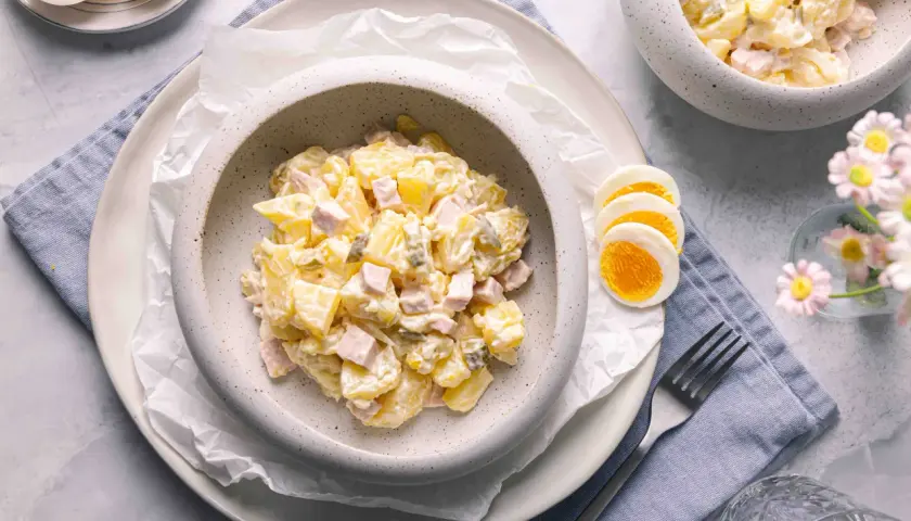 Ein cremiger Kartoffelsalat mit Mayonnaise, Schinken und Gewürzgurken, serviert mit gekochten Eiern. Ein klassisches Kartoffelsalat Rezept mit Mayonnaise.