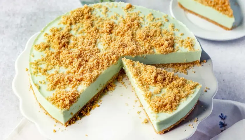 Eine cremige Philadelphia Torte Waldmeister mit knuspriger Streuselhaube, ein Stück ist bereits angeschnitten.