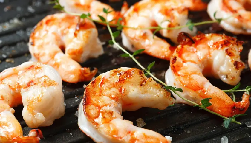 Saftige black tiger Garnelen grillen auf einer heißen Grillplatte, garniert mit frischem Thymian.