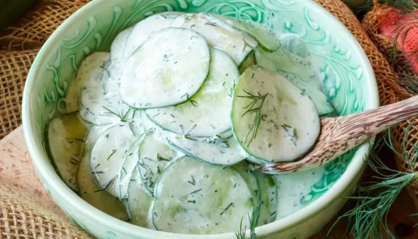 Frischer gurkensalat mit saurer sahne und Dill, serviert in einer grünen Schüssel mit einem Holzlöffel.