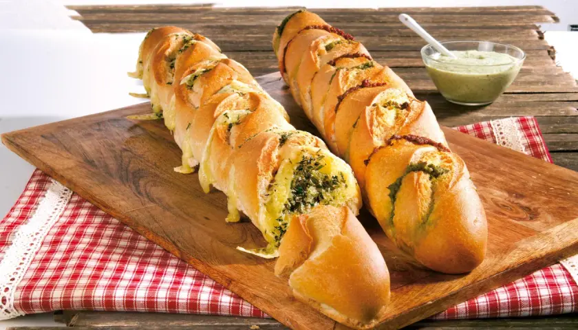 Zwei knusprige Baguettes zum Grillen, gefüllt mit Kräutern und Käse, daneben eine Schale Dip.