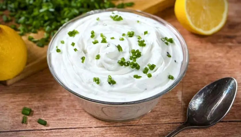 Cremige Sour Cream, frisch zubereitet, mit Schnittlauch garniert. Dazu Zitrone und ein Löffel – perfekt zum Sour Cream selber machen.