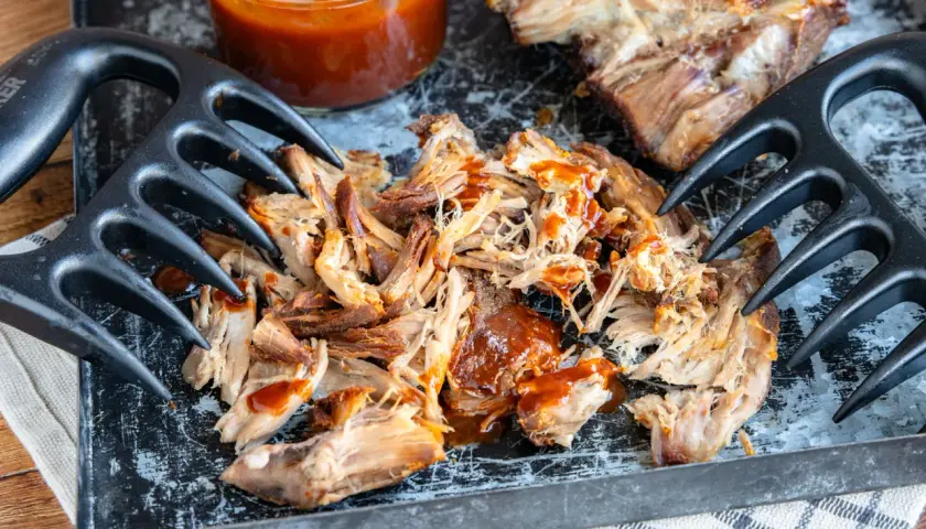 Zartes pulled pork sous vide, mit BBQ-Sauce beträufelt, bereit zum Zerreißen mit Fleischgabeln.