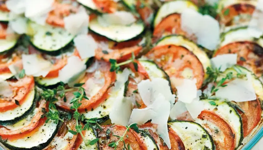 Schicht für Schicht ein Genuss: Ein köstlicher Tomaten Zucchini Auflauf, garniert mit Parmesan und frischen Kräutern.