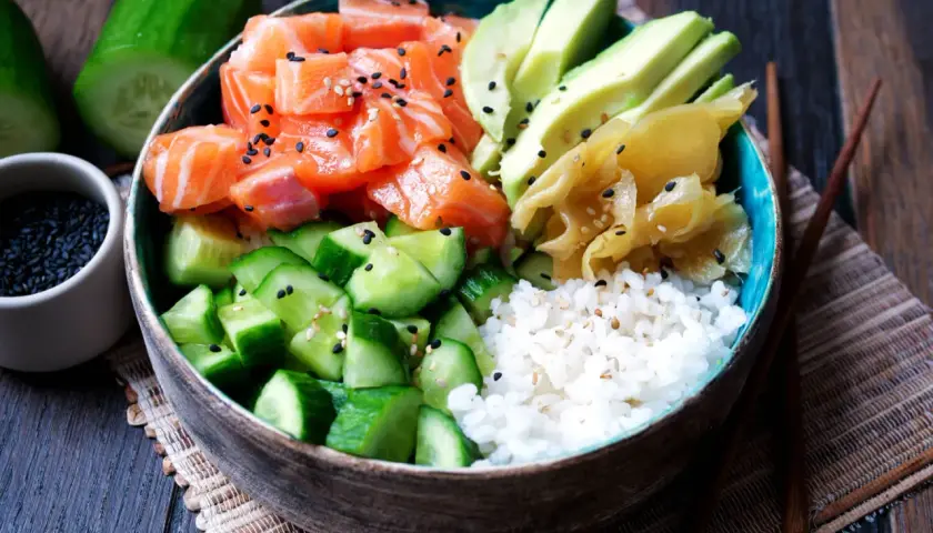 Eine bunte Sushi Bowl mit Lachs, Avocado, Gurke und Reis. Sesamkörner bestreuen die frischen Zutaten.