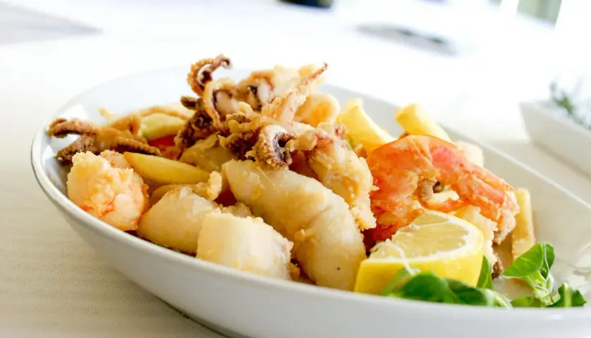 Knuspriges Fritto Misto mit Garnelen, Tintenfischringen und Fischstücken, garniert mit Zitrone und frischen Kräutern.